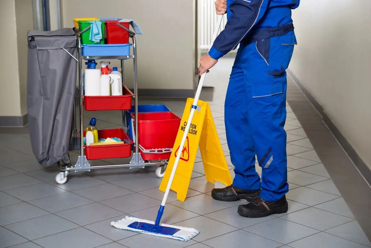 A man in blue overalls mopping the floor.